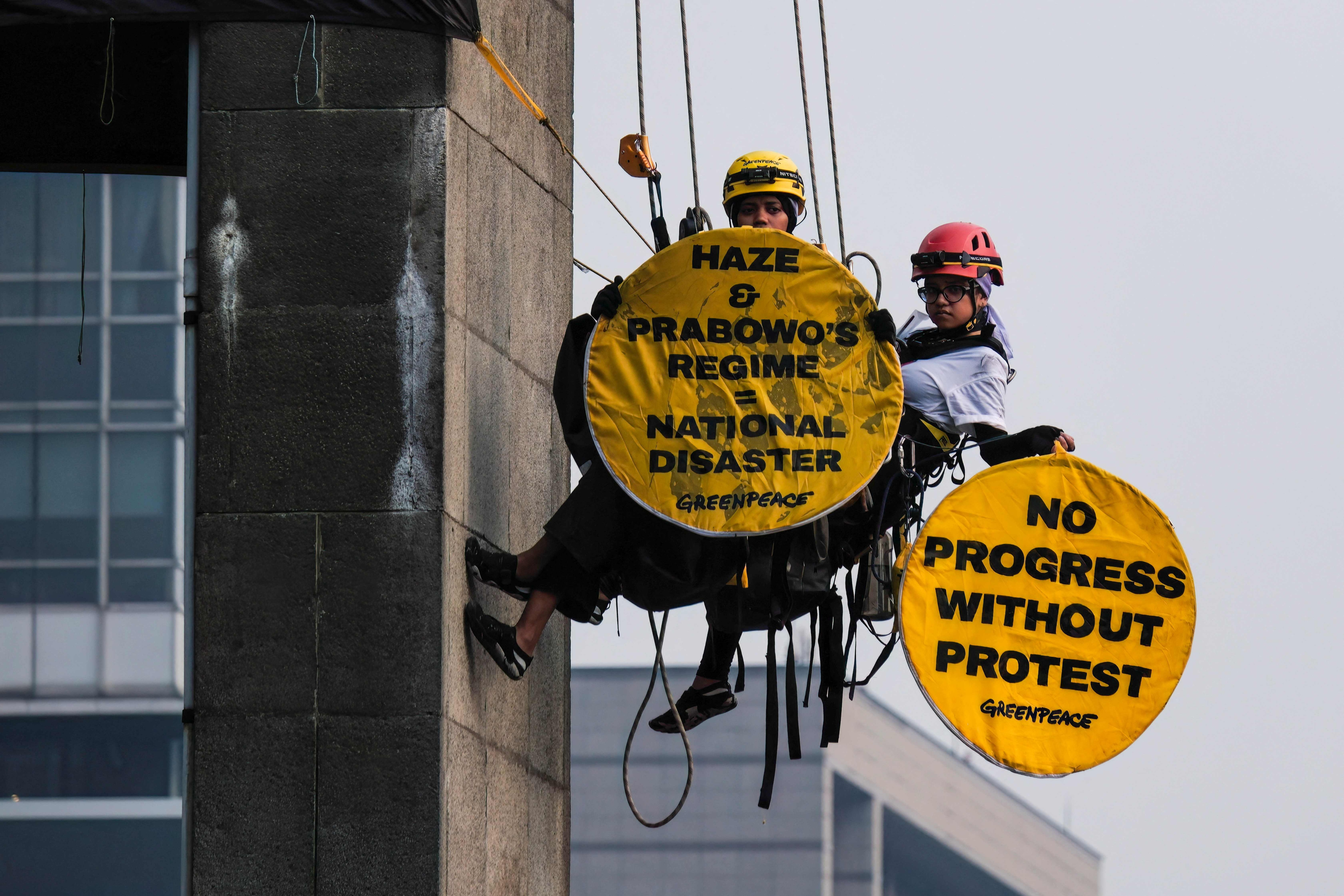 Greenpeace Indonesia activists hanging from the Welcome Statue at the Hotel Indonesia Roundabout hold protest signs in Jakarta on October 20, 2026. (AFP)