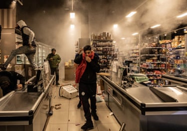 Protesters inside a smoke-filled, ransacked Milan shop, one covering his face with red cloth