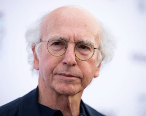 Larry David, bald with grey hair and round glasses, looks at the camera with a neutral expression