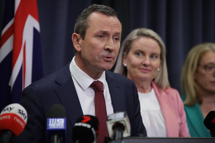 A close-up shot of WA Premier Mark McGowan speaking at a media conference indoors in front of a blonde woman.