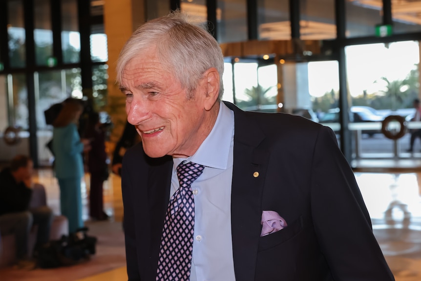 An old man in a suit smiles.
