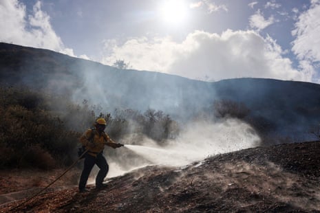 A firefighter sprays water from a hose onto a smoking hillside at the Bike fire