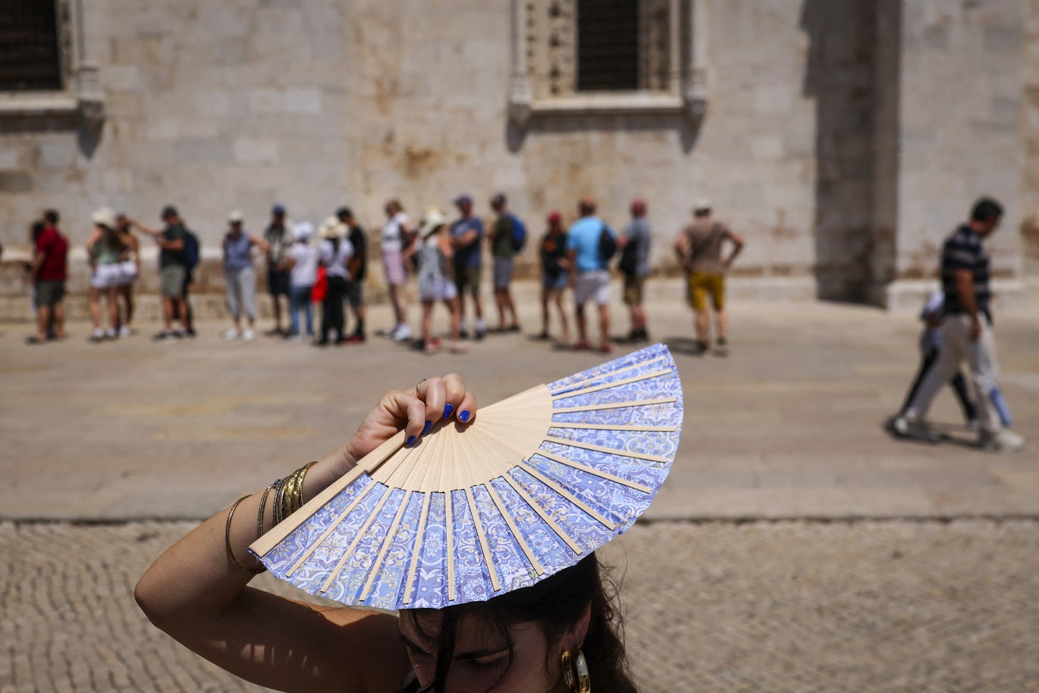 A woman shades her head with a fan in front of Jeronimos Monastery in Belem, during a heatwave in Lisbon on May 27, 2026.