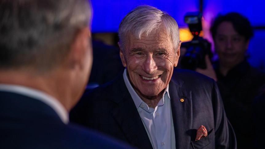 A smiling Kerry Stokes in headshot in a dark conference room