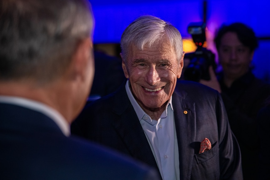 A smiling Kerry Stokes in headshot in a dark conference room